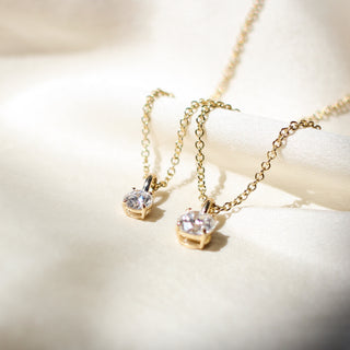 Two Round Lab Diamond Necklaces in yellow gold on white fabric, smaller one in focus