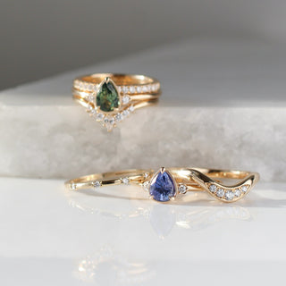  Pear Cut Green Sapphire ring stacked with diamond crown and diamond gold bands on marble along with Blue Sapphire ring paired with two diamond gold bands with reflections front view