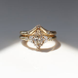 Yellow gold ring with a champagne marquise cut diamond and white diamond clusters stacked with pointed wedding band with three round white diamonds, front view