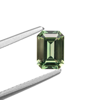 Green emerald cut sapphire in tweezers