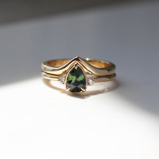 Three stone yellow gold ring with pear cut green sapphire and white round diamond accents stacked with pointed wedding band, front view