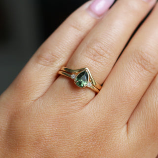Three stone yellow gold ring with pear cut green sapphire and white round diamond accents stacked with pointed wedding band, on hand