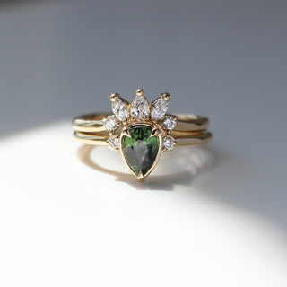 Three stone yellow gold ring with pear cut green sapphire and white round diamond accents stacked with curved wedding band with white diamond crown, front view