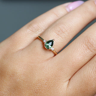 Three stone yellow gold ring with pear cut green sapphire and white round diamond accents, on hand