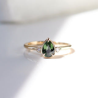 Three stone yellow gold ring with pear cut green sapphire and white round diamond accents, front view