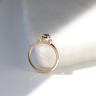 Three stone yellow gold ring with pear cut green sapphire and white round diamond accents, side view