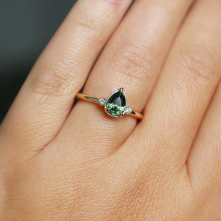 Three stone yellow gold ring with pear cut green sapphire and white round diamond accents, on hand