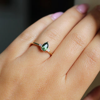 Three stone yellow gold ring with pear cut green sapphire and white round diamond accents, on hand