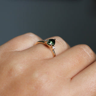 Three stone yellow gold ring with pear cut green sapphire and white round diamond accents, side view on hand