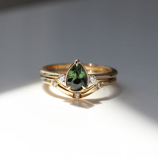 Three stone yellow gold ring with pear cut green sapphire and white round diamond accents stacked with curved wedding band with three round diamonds, front view