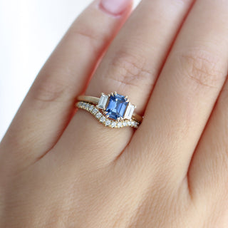 Emerald cut blue sapphire ring with baguette side stones in yellow gold stacked with curved diamond pave wedding band, on hand