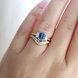 Emerald cut blue sapphire ring with baguette side stones in yellow gold stacked with curved diamond pave wedding band, on hand