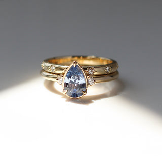 Three stone yellow gold ring with pear cut blue sapphire and white round diamond accents stacked with straight wedding band with star-set white round diamonds, front view