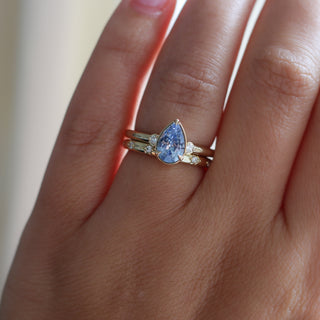 Three stone yellow gold ring with pear cut blue sapphire and white round diamond accents stacked with straight wedding band with star-set white round diamonds, on hand