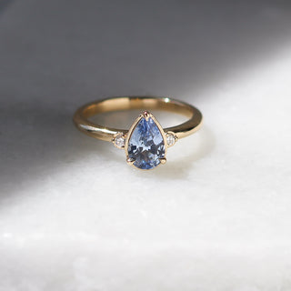 Three stone yellow gold ring with pear cut blue sapphire and white round diamond accents, front view