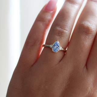 Three stone yellow gold ring with pear cut blue sapphire and white round diamond accents, on hand