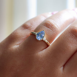Three stone yellow gold ring with pear cut blue sapphire and white round diamond accents, on hand