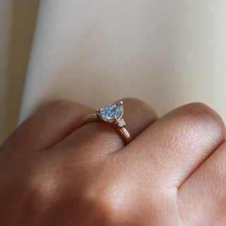 Three stone yellow gold ring with pear cut blue sapphire and white round diamond accents, side view on hand