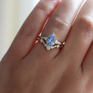 Three stone yellow gold ring with pear cut blue sapphire and white round diamond accents stacked with curved wedding band with five round white diamonds, on hand