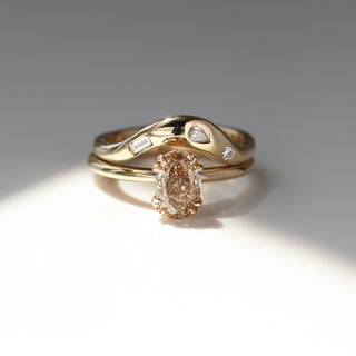 Yellow gold solitaire engagement ring with an oval champagne diamond stacked with a large wave style wedding band with organic white diamond placements, front view