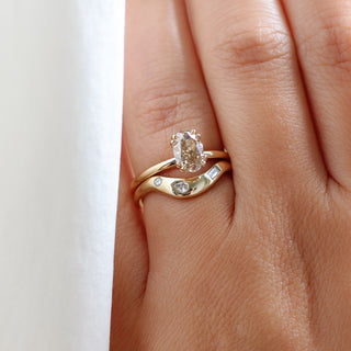 Yellow gold solitaire engagement ring with an oval champagne diamond stacked with a large wave style wedding band with organic white diamond placements, on hand