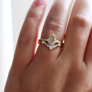 Yellow gold solitaire engagement ring with an oval champagne diamond stacked with a curved wedding band with five white round diamonds, on hand