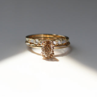 Yellow gold solitaire engagement ring with an oval champagne diamond stacked with a straight wedding band with alternating round and baguette white diamonds, front view