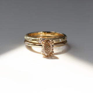 Yellow gold solitaire engagement ring with an oval champagne diamond stacked with a straight wedding band with star-set round white diamonds, front view