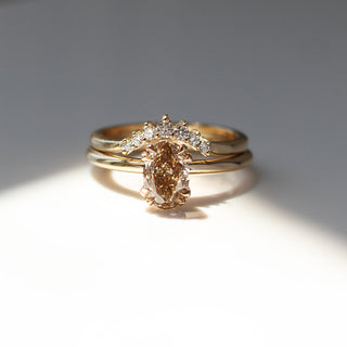 Yellow gold solitaire engagement ring with an oval champagne diamond stacked with a curved wedding band with a crown of round white diamonds, front view