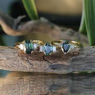 Lagoon Pear Green Sapphire Ring with Oval and Emerald Cut rings on a branch with reflections in glass front view