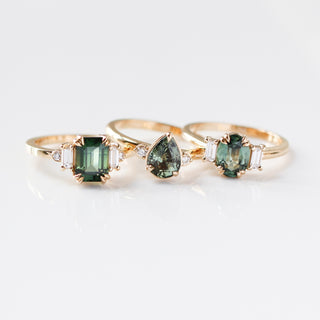 Trilogy Oval Green Sapphire Ring stacked with Emerald and Pear Cut Sapphire Rings in sunlight with reflections detailed top front view