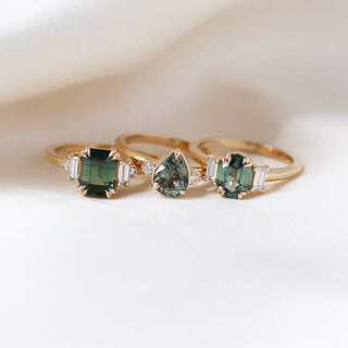 Trilogy Oval Green Sapphire Ring stacked with Emerald and Pear Cut Sapphire Rings on fabric front view