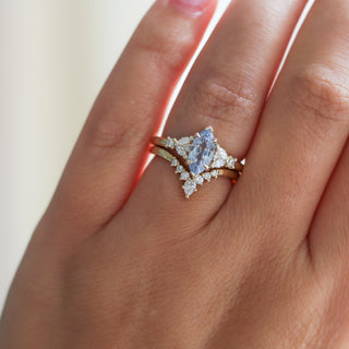 Yellow gold ring with a light blue marquise cut sapphire and white diamond clusters stacked with a pointed wedding band with white diamonds, on hand
