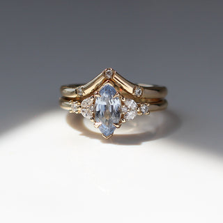 Yellow gold ring with a light blue marquise cut sapphire and white diamond clusters stacked with a pointed wedding band with three round white diamonds, front view