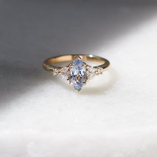 Yellow gold ring with a light blue marquise cut sapphire and white diamond clusters, front view