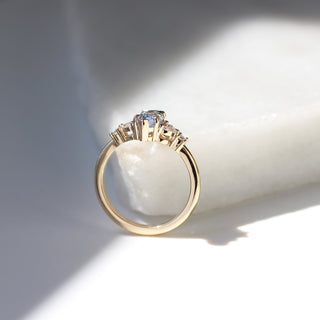Yellow gold ring with a light blue marquise cut sapphire and white diamond clusters, side view