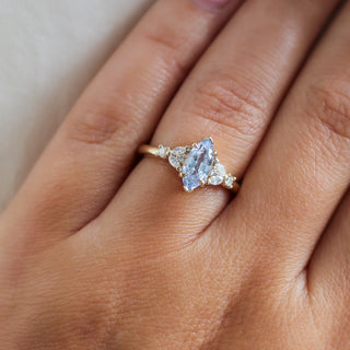 Yellow gold ring with a light blue marquise cut sapphire and white diamond clusters, on hand