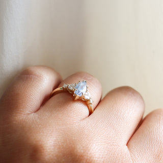 Yellow gold ring with a light blue marquise cut sapphire and white diamond clusters, side view on hand