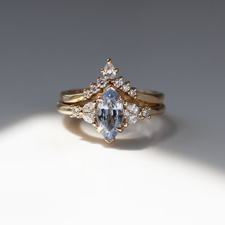 Yellow gold ring with a light blue marquise cut sapphire and white diamond clusters stacked with a pointed wedding band with white diamonds, front view