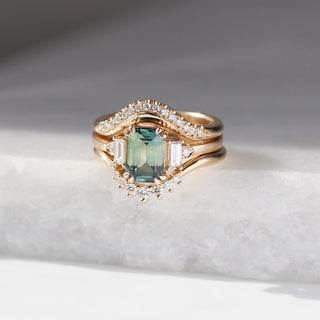 Emerald Cut Teal Sapphire Ring stacked in between 2 gold diamond bands on marble front view 