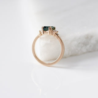 Emerald cut teal sapphire ring with baguette and round diamond side stones in yellow gold, side view