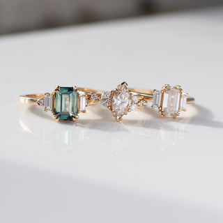 Emerald Cut Teal Sapphire Ring paired with Trilogy and Folia Gold diamond rings with reflections front view