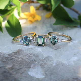 Misceo Emerald Cut Green Sapphire Ring with Pear and Oval Cut rings on a stone with yellow flowers top front view
