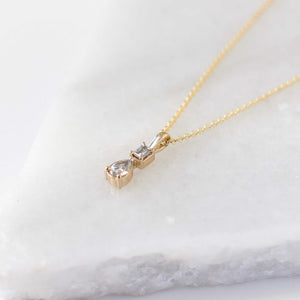 Emerald cut and pear diamond necklace in yellow gold on marble side view 