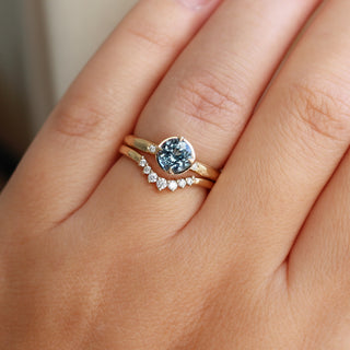 Round blue spinel ring in yellow gold stacked with curved diamond wedding band, on hand