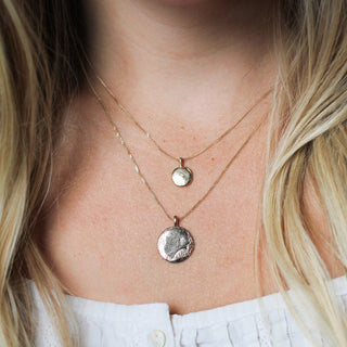 Close-up of a person wearing two gold necklaces with circular pendants.