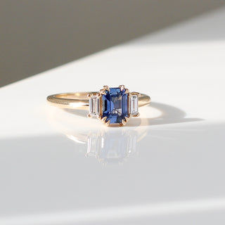 Blue emerald cut sapphire and diamond ring on white background, quarter view