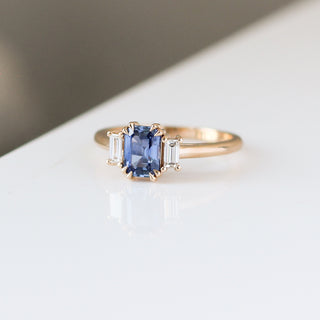 Blue emerald cut sapphire and diamond ring on white background, quarter view