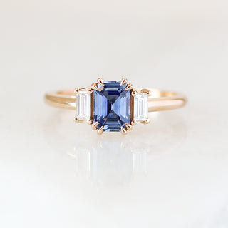 Blue emerald cut sapphire and diamond ring on white background, front view