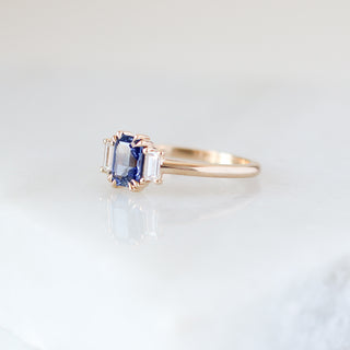 Blue emerald cut sapphire and diamond ring on white background, quarter view